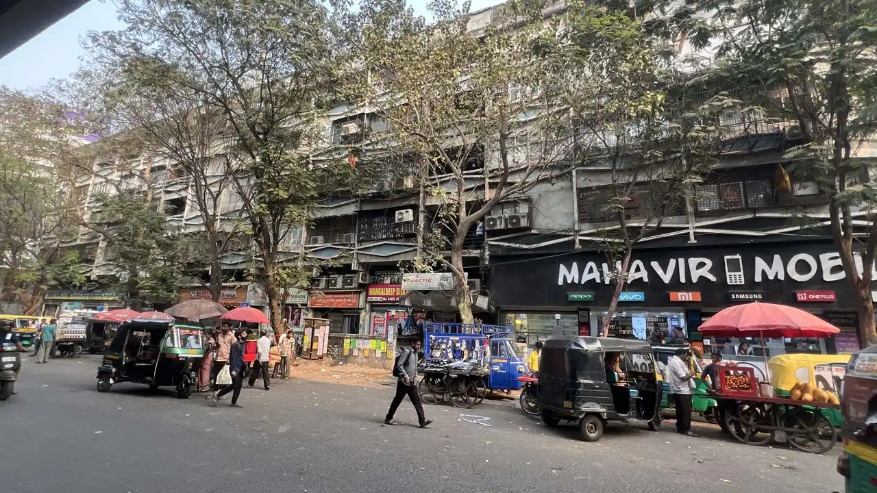 Street view of Reshamwala Textile Market on Ring Road, Surat, showing textile shops, auto rickshaws, and busy wholesale market activity.