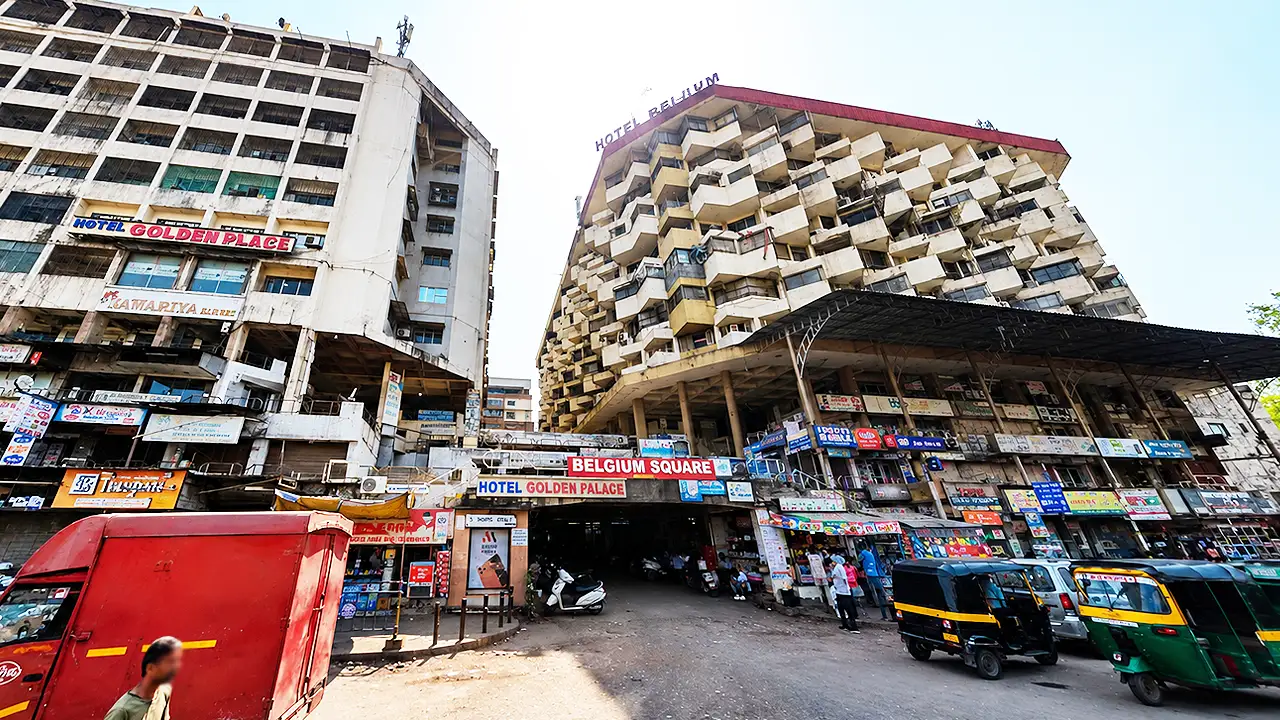 Street level view of Belgium Square with Belgium Tower on the right side at Ring Road in Surat, Gujarat, showing the entrance, commercial buildings, and textile market area.