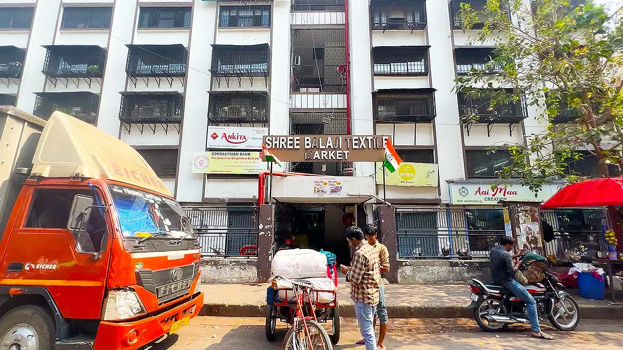 Front entrance of Shree Balaji Textile Market on Ring Road in Surat with transport vehicles and wholesale textile shops.