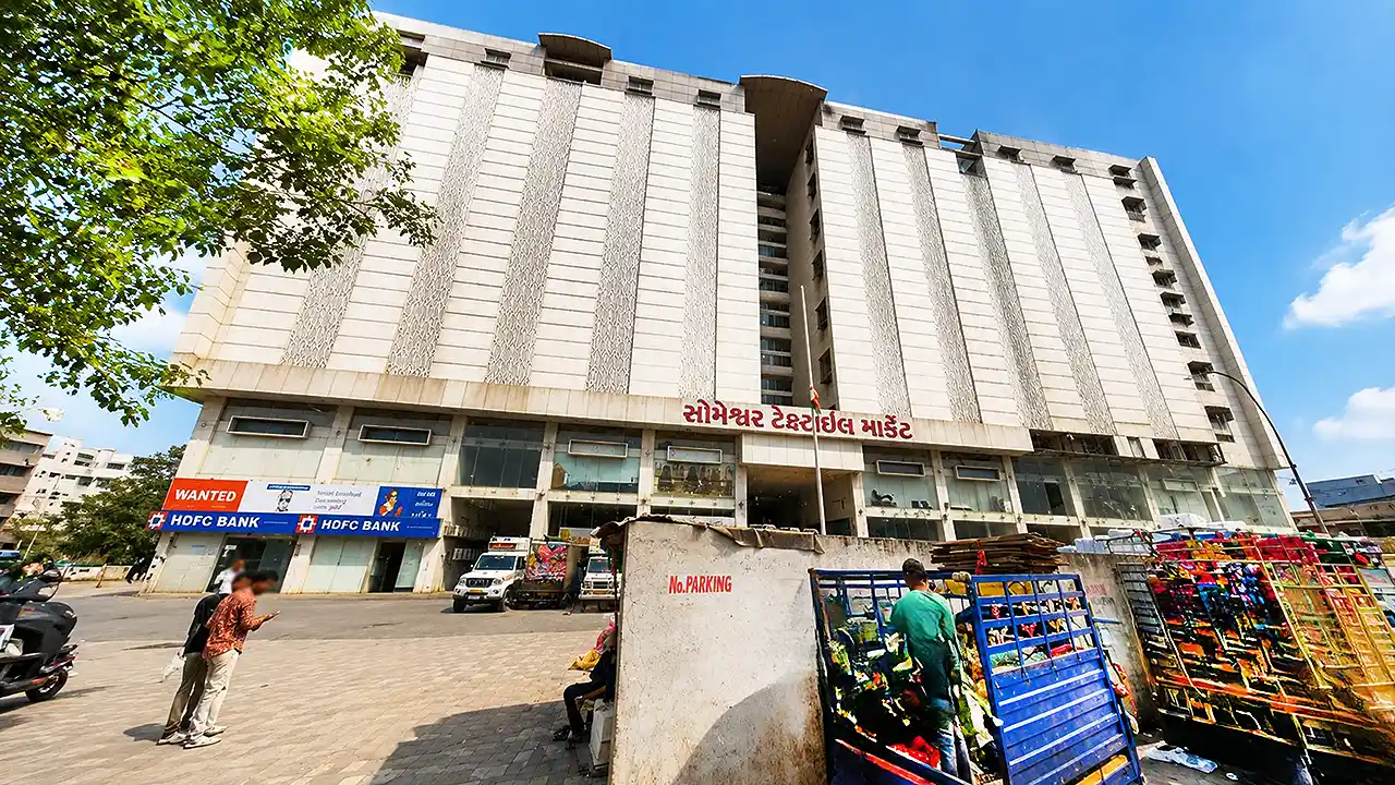 Exterior view of Someshwar Textile Market 1 building with HDFC Bank, transport vehicles and textile goods outside